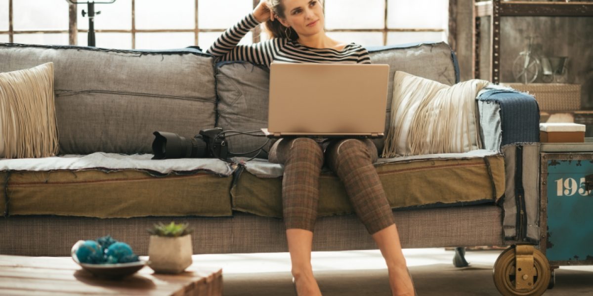 Thoughtful young woman with dslr photo camera using laptop in loft apartment